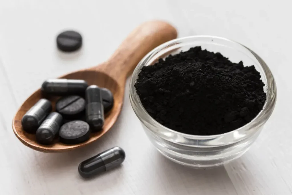 Activated Charcoal supplements in a spoon and powder in the bowl